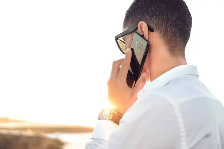 Personne notant un numéro inconnu près d’un smartphone et d’un annuaire