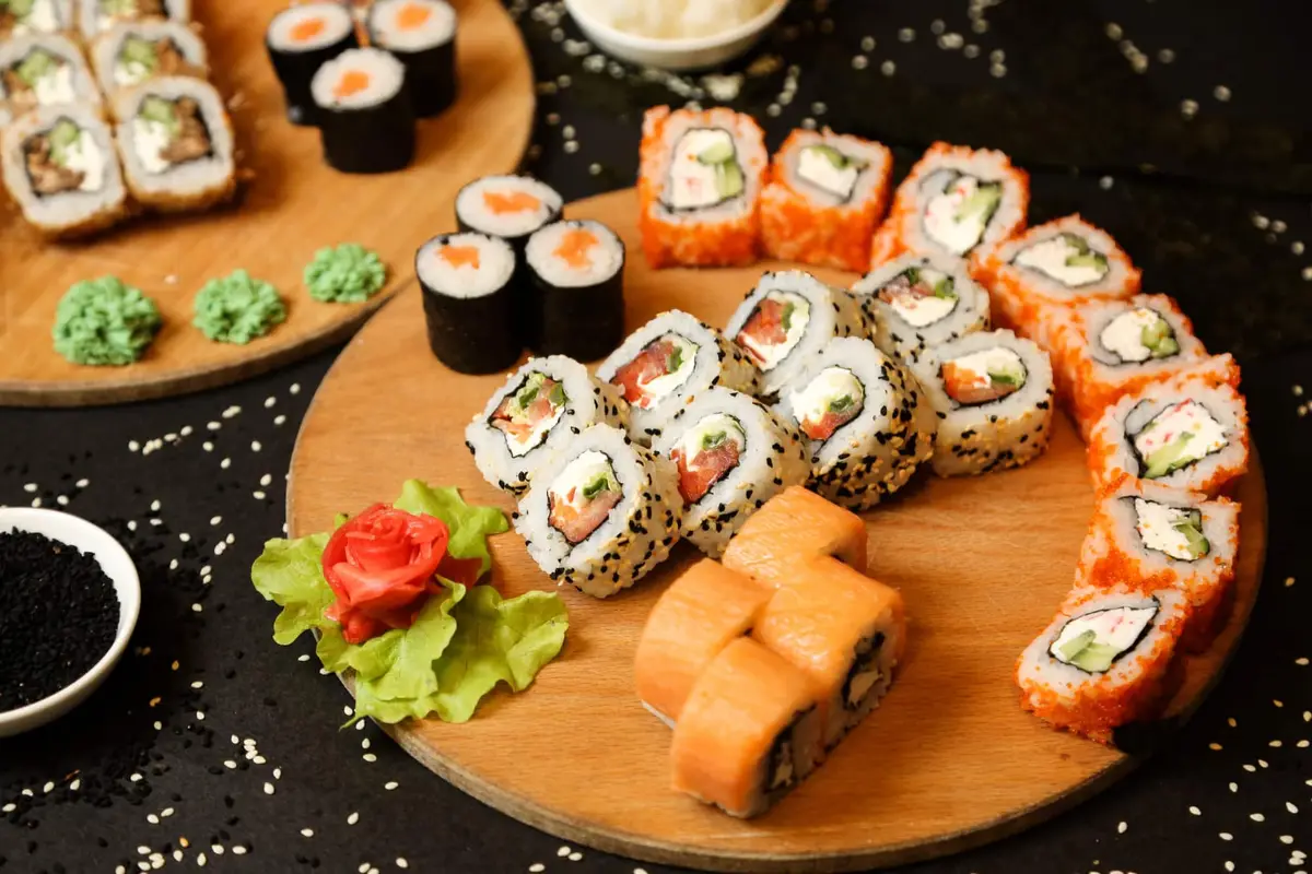 Mains préparant des makis au saumon cuit sur une natte en bambou