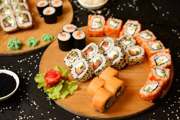 Mains préparant des makis au saumon cuit sur une natte en bambou