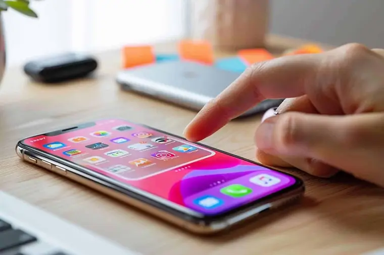 Main utilisant un iPhone près de documents et d’un dossier de classement
