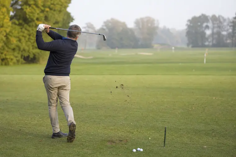 Golfeur réalisant un swing de fer équilibré sur un practice enherbé