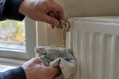 Main ouvrant le purgeur d’un radiateur blanc avec une clé, chiffon placé dessous