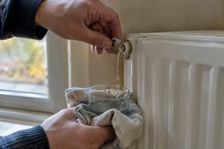 Main ouvrant le purgeur d’un radiateur blanc avec une clé, chiffon placé dessous