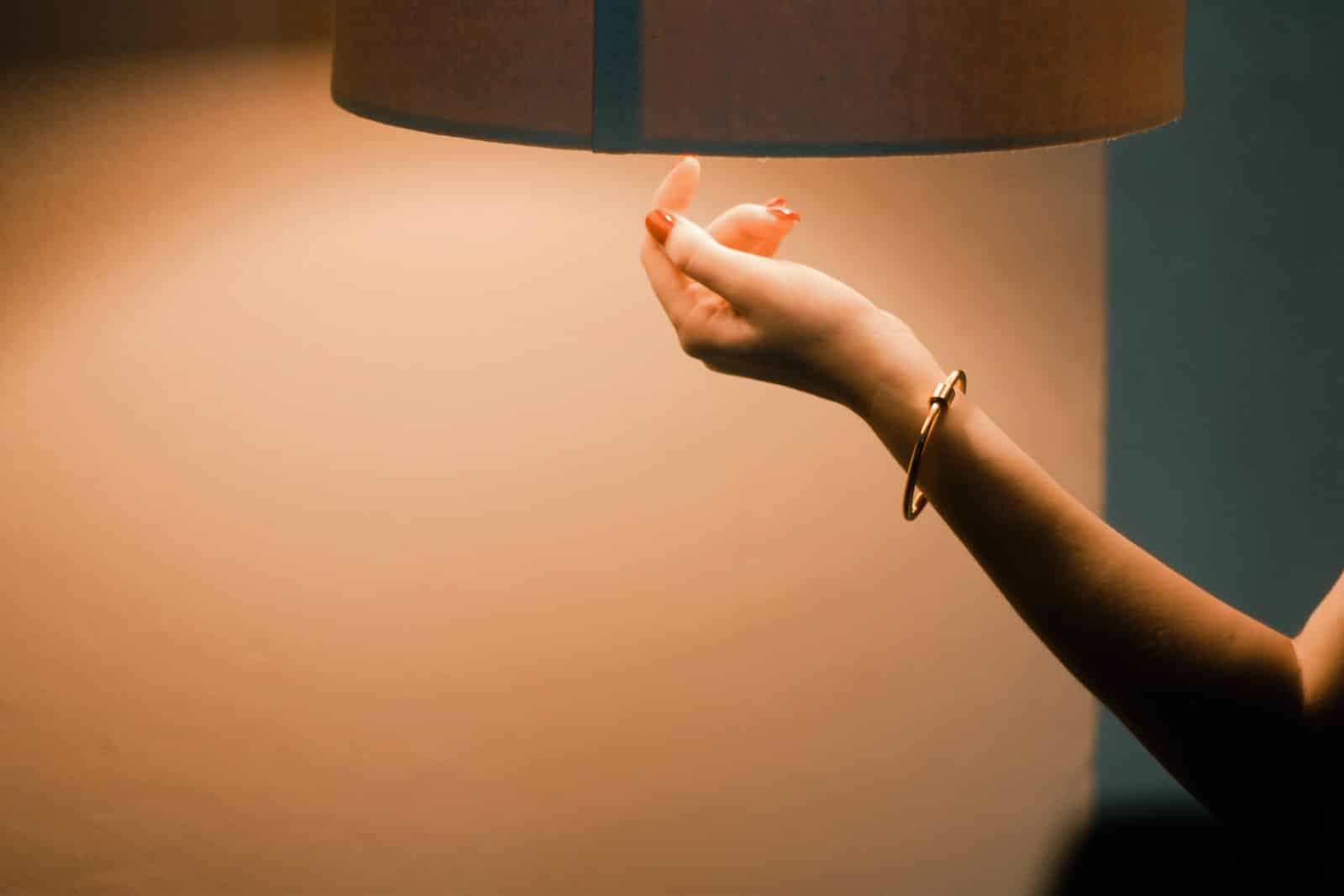 person wearing gold bracelet holding blue table lamp